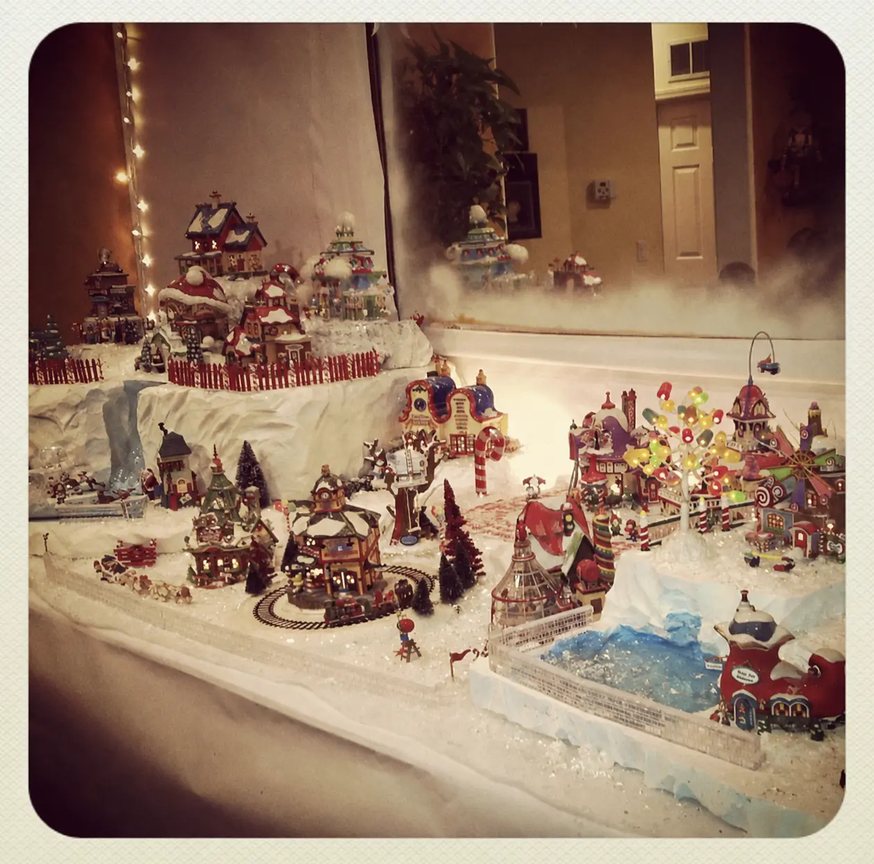 Homemade Christmas village on carved foam snow with a lit ice rink, a running train, and fog drifting across the display.